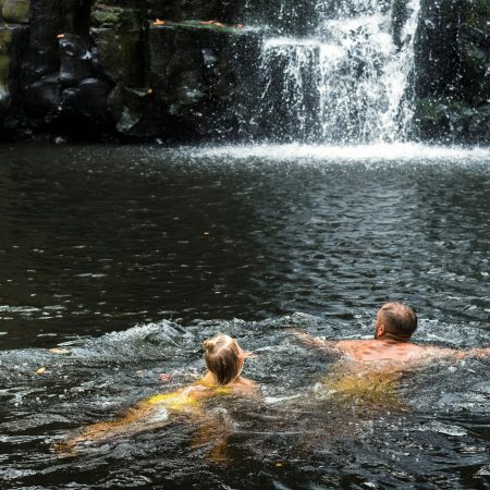 A man and a girl are swimming in a waterfall. People at the cave waterfall. Bathing