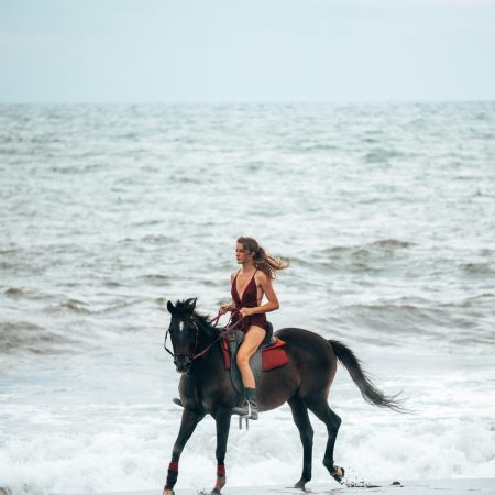 Girl in red dress rides horse on the beach