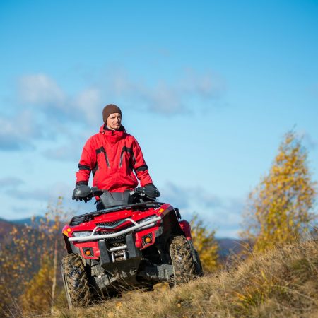 Guy on the red ATV quad bike in the autumn landscape nature.