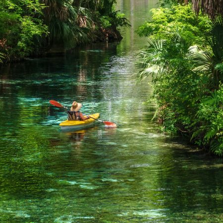 Woman in sun hat paddling in a yellow kayak on a spring fed river in Florida, surrounded by nature